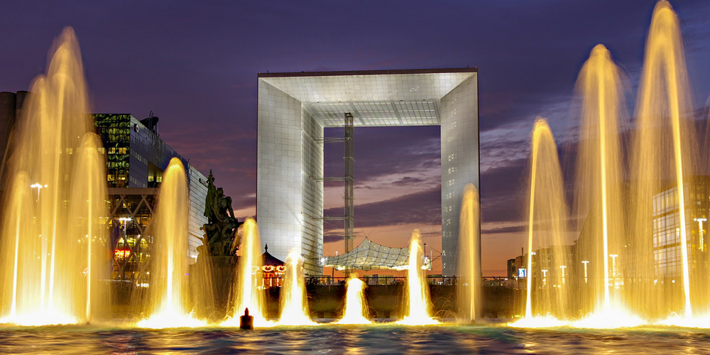 The Grande Arche at La Defense, flanked by lighted fountains, against the night sky